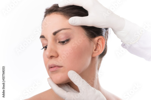 Beauty treatment of the young beautiful female face, doctor's hand in gloves touch face of beautiful young woman isolated on white.