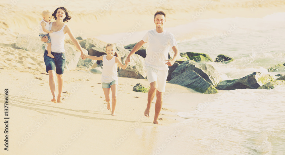 Cheerful family of four running on sandy beach