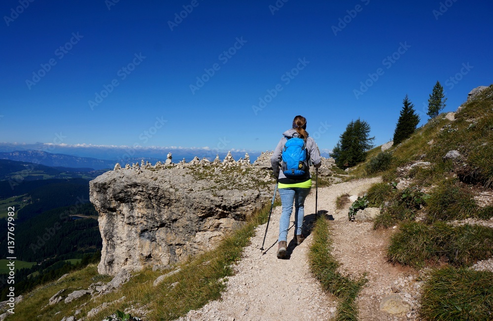 Wanderin unterwegs mit Rucksack und Stöcken auf Weg entlang Felshang / Rosengarten Schlern Naturpark