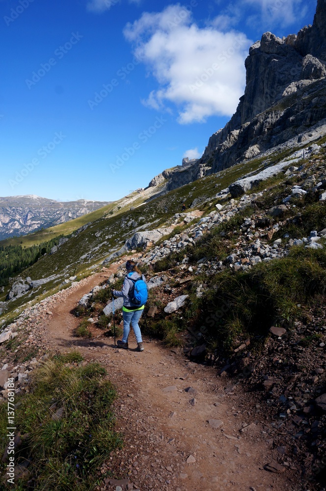 Fototapeta premium Wanderin unterwegs mit Rucksack und Stöcken auf Weg entlang Felshang / Rosengarten Schlern Naturpark