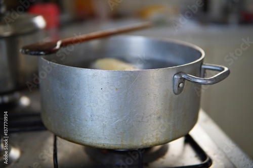 Cooking phase of dumplings in the boiling water set in aged silver aluminum pot on the gas cooker with hot steam leaving the top of the cooking pot over wooden spoon