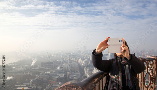 woman taking a selfie from the rooftop of St Paul's Cathedral on a foggy day in London - city break - tourism concept