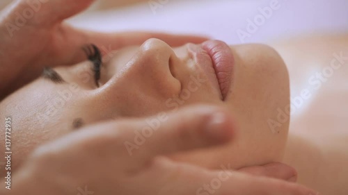 Female's hands massaging beautiful face of younf woman in slowmotion