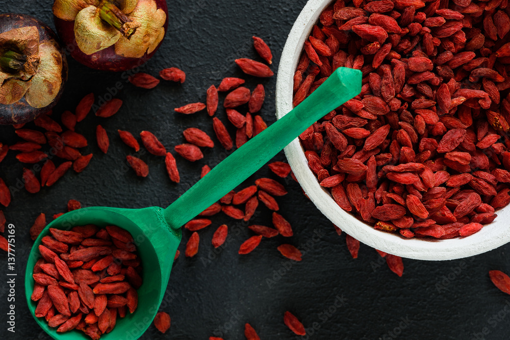 Red goji berries top view on dark color table in green spoon with mangosteens