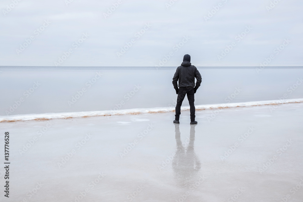 Young man on the ice at the seashore feels the freedom in winter afternoon.