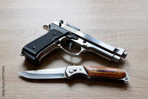 Silver metallic pistol with knife on wooden board.