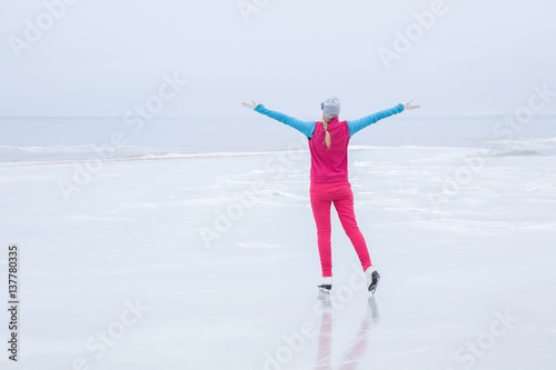 Woman with white skates skating and looking around on the ice area at the seashore in winter day. Foggy air. In front of view opens infinity. Enjoying weekends activities outdoor in cold weather.