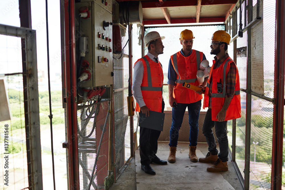 Fototapeta premium Group of workmen standing in industrial elevator discussing construction site progress