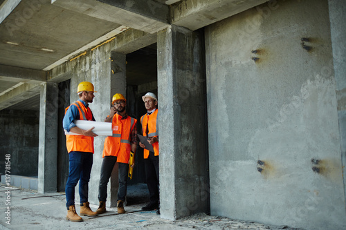 Two workmen showing unfinished floors in high rise building to executive supervisor on construction site