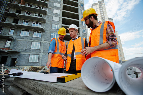 Low angle portrait of two workmen showing apartment building blueprints to inspector on construction site photo