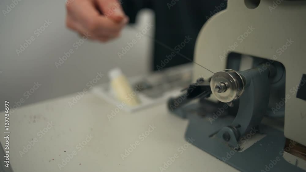 Woman pulls black thread on the spool while it spins in sewing workshop Woman pulls black thread on the spool while it spins in sewing workshop