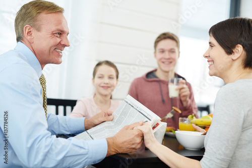 Happy young couple looking at one another by breakfast with their kids on background