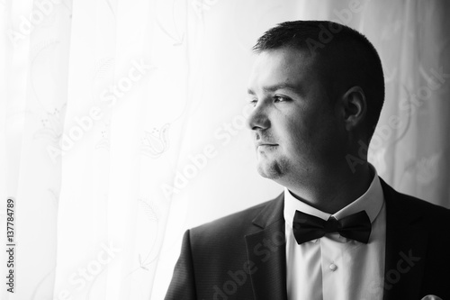 Portrait of young beard groom on his room at wedding morning. Black and white photo