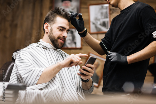 Gloved hairdresser serving his client with smartphone