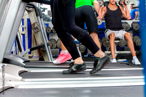 Treadmill and group of legs wearing sneakers running on group people at sport gym background.