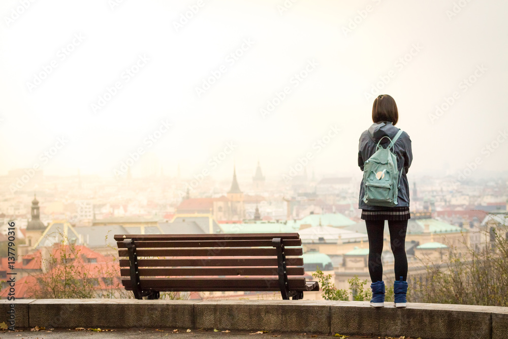 Young japanese girl stay near bench and watching on panorama of Prague.