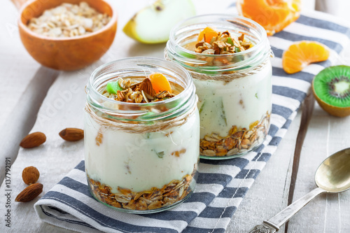 Healthy homemade granola with yogurt and fruits in a rustic jar. Traditional American food on a table. Classic snack. Close-up shot.