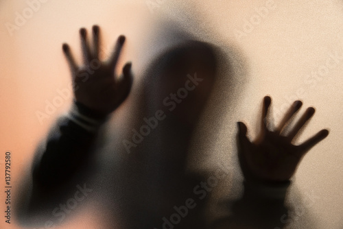 Shadow blur of horror man in jacket with hood.Hands on the glass.Dangerous man behind the frosted glass.Mystery man.Halloween background.Blur picture.