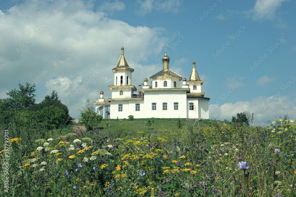 White orthodox church with domes amidst summer meadow