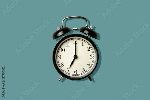 black vintage alarm clock on green color background with sharp shadow