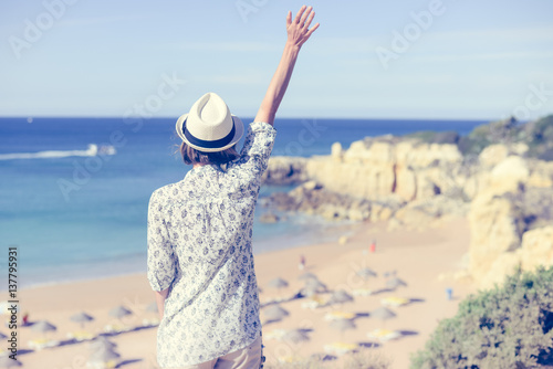 Back view of beautiful woman standing on beach in summer  blue sunny sky outdoors background. Holiday location