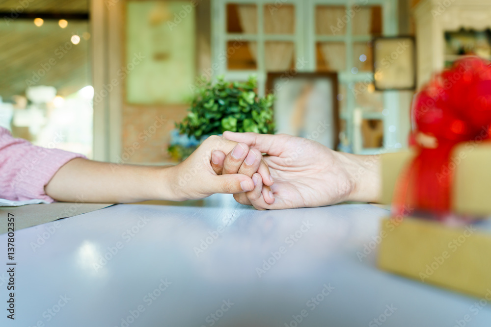 A couple holding hands each other in restaurant with a golden gift box with red ribbon. A couple holding hands each other in restaurant with a golden gift box with red ribbon.