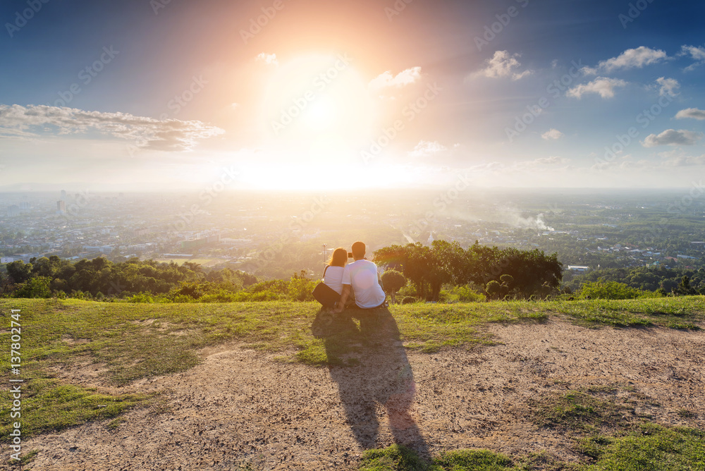 Romantic of couple love sitting on the cliff looking sunset at mountain, take a selfie.
