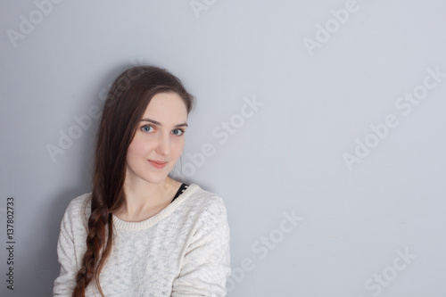 girl with a long braid standing at the gray wall and looking up modestly