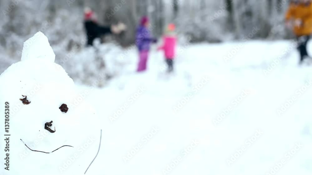 Snowman built in winter forest. Large family with kids plays snowballs on the background, blurred. Lifestyle, fun outdoors, winter activities. Happy healthy active children with mom and dad Snowman built in winter forest. Large family with kids plays snowballs on the background, blurred. Lifestyle, fun outdoors, winter activities. Happy healthy active children with mom and dad