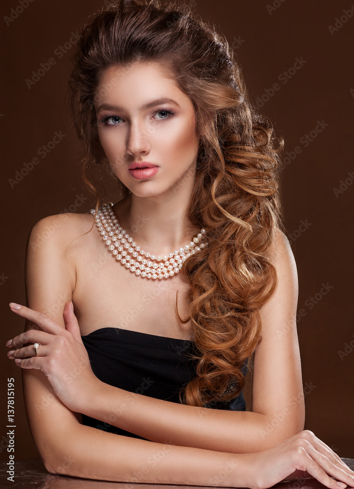 Beautiful elegant woman in pearl necklace, long curly tress over black background. Fashion glamour portrait.