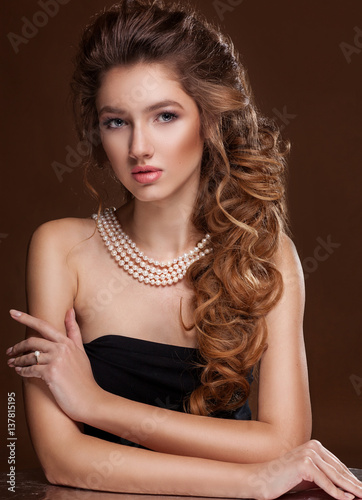 Beautiful elegant woman in pearl necklace  long curly tress over black background. Fashion glamour portrait.