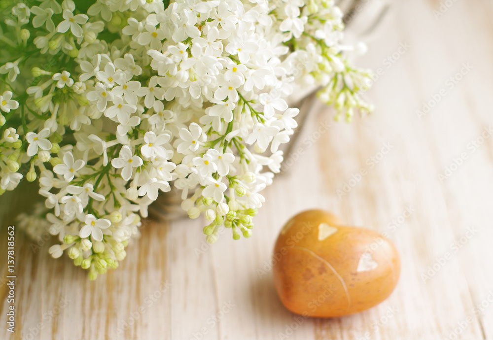 Bouquet of a white lilac in a basket and heart with stones on a wooden surface, soft focus. Spring romantic bouquet. Greeting card for lovers, friendship or valentine's day.