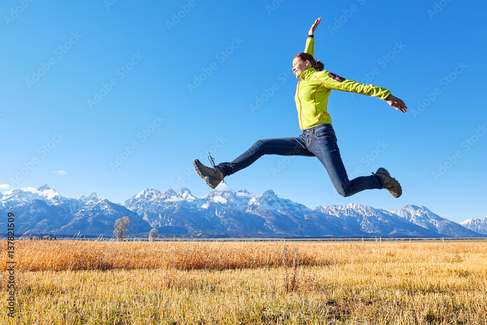 Happy young woman jumping on a meadow, Grand Teton mountain range in distance, Wyoming, USA. Happy young woman jumping on a meadow, Grand Teton mountain range in distance, Wyoming, USA.