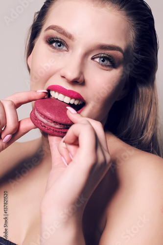 beautiful young woman with dark hair eating sweet macaroon