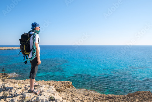 Traveler bearded man with backpack stands on a rocky seashore