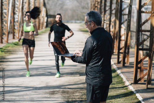 coach staff of running with laptop and 2 runners