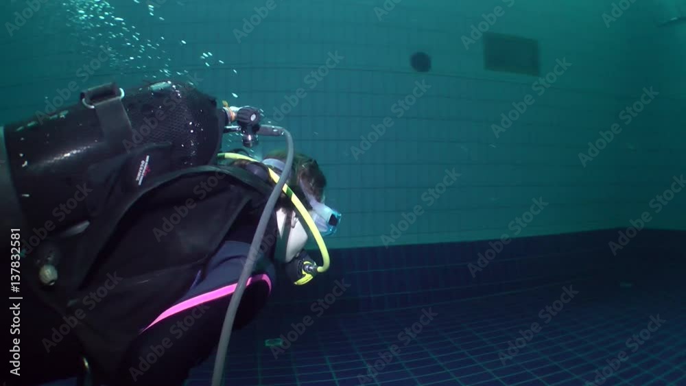 Two girls diver in a dive gear swimming using only one scuba gear for breathing.
