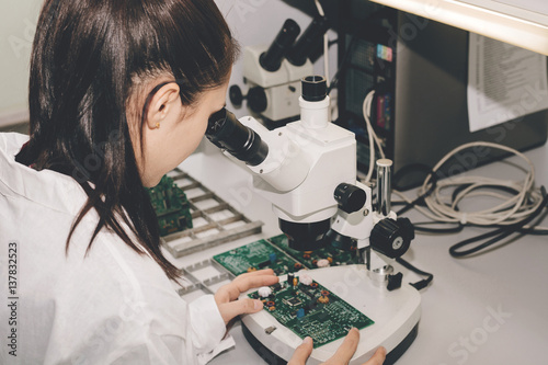 Beautiful female computer expert professional technician examining board computer in a laboratory in a factory. Troubleshooting. Technical support. Engineering. Manufacturing.