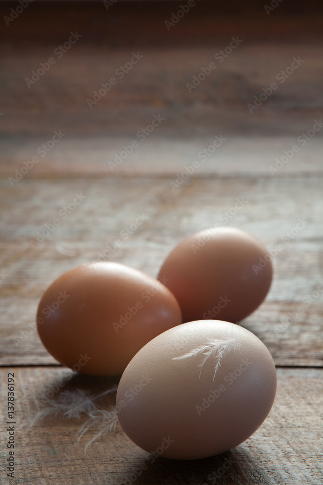 Vertical Close Up of Three Fresh Farm Chicken Eggs and Feathers on a Dark Brown Rustic Wooden Farm Table with Copy Space Vertical Close Up of Three Fresh Farm Chicken Eggs and Feathers on a Dark Brown Rustic Wooden Farm Table with Copy Space