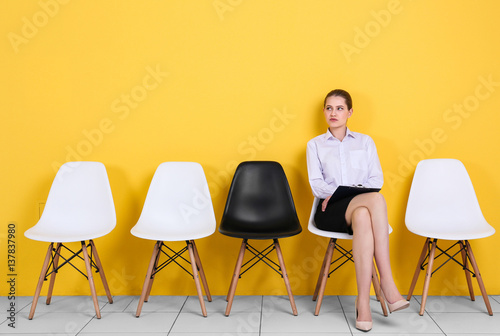 Young woman waiting for job interview on yellow wall background