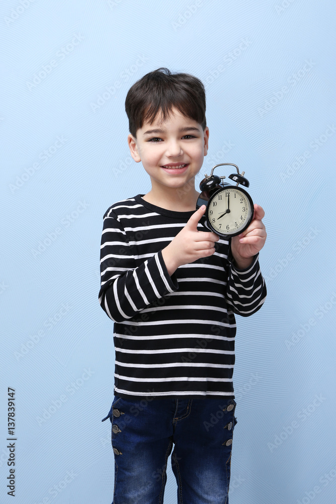 Fototapeta premium Cute little boy with alarm clock on color background