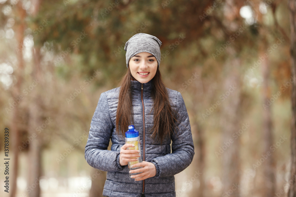 Young woman wearing sportswear with bottle on winter park background Young woman wearing sportswear with bottle on winter park background