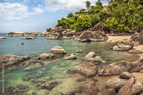 Tropical beach with hill and palm trees in lagoon with transparent turquoise water and round stones nearby hotel 