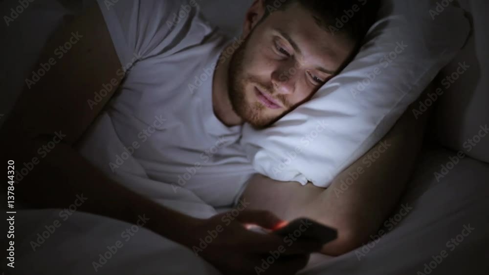 young man with smartphone in bed at night young man with smartphone in bed at night