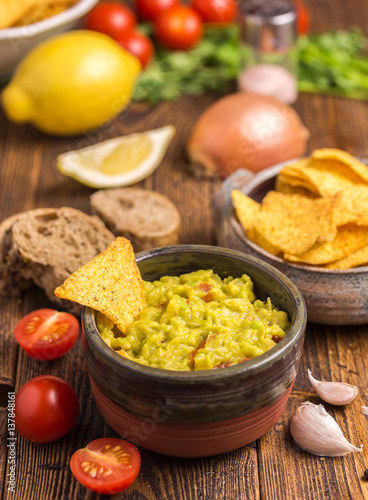 Guacamole in brown bowl with tortilla chips on natural wooden desk.
