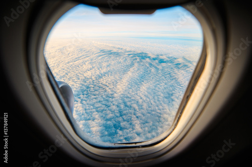 Views from the window of an airplane flying towards Iceland. Through the window you can see the clouds above the sea from the sky. 