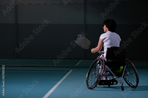 Disabled mature woman on wheelchair playing tennis on tennis court. © Nejron Photo