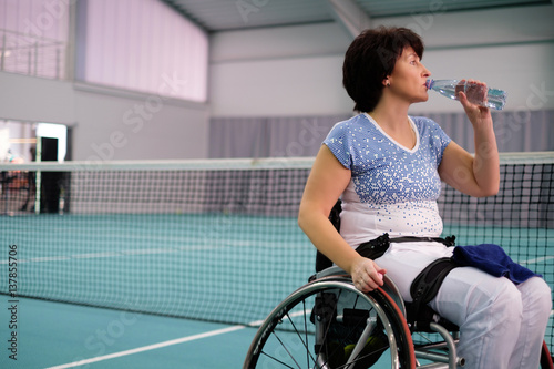 Thirsty disabled mature woman on wheelchair at tennis court.