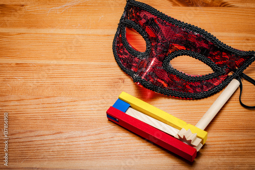 Judaism and religious holiday with wooden noisemaker or gragger (a traditional toy) for purim celebration holiday (jewish holiday) and a red mask on wooden background photo