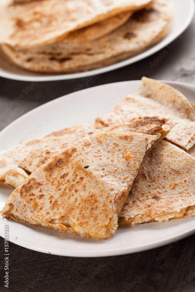 Crispy Quesadilla with Chicken and Sauce on white plate on dark wooden background angled shot Crispy Quesadilla with Chicken and Sauce on white plate on dark wooden background angled shot